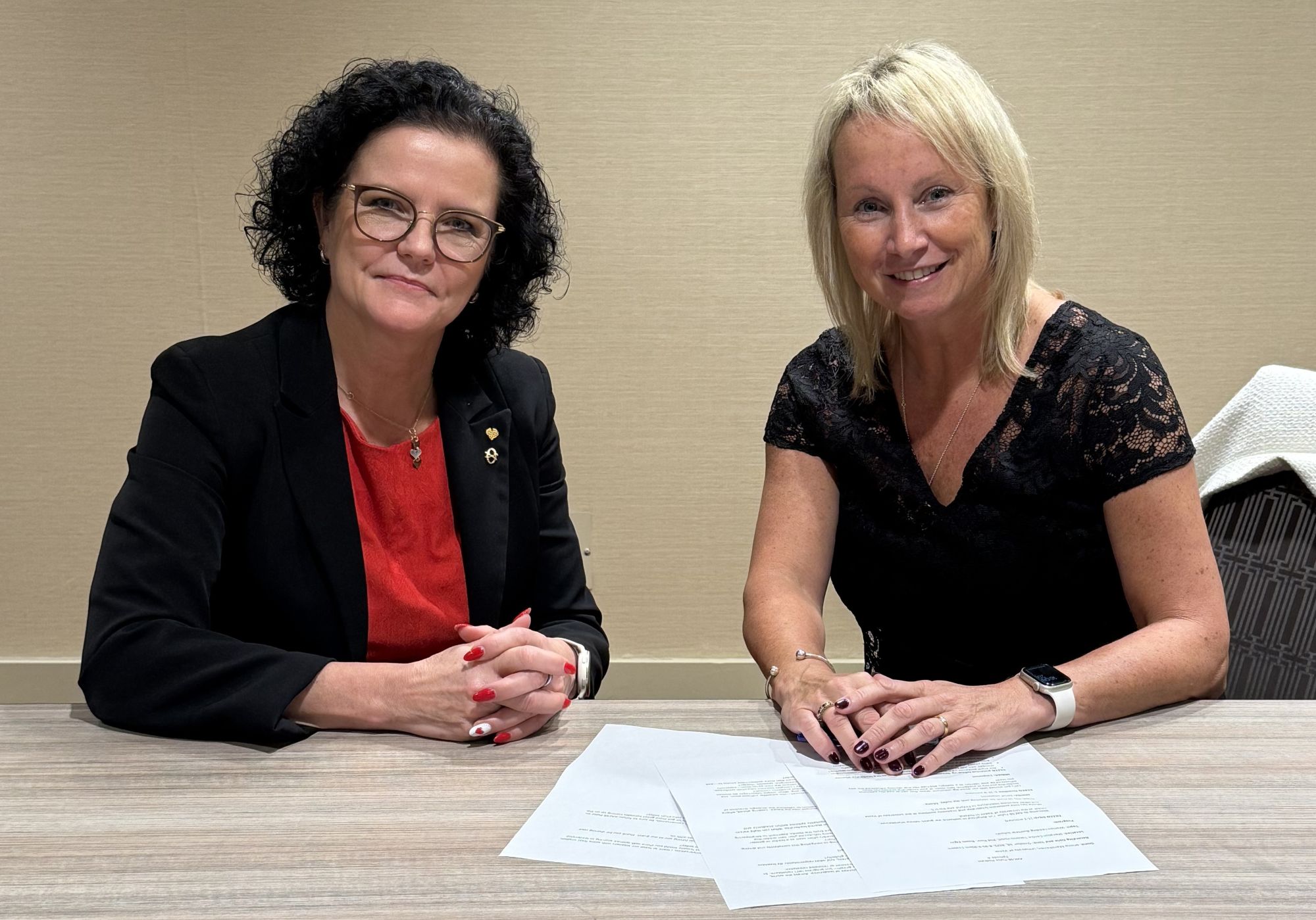 Minna Martikainen (left) and Eileen McAuliffe (right) sitting at a table with papers laid out in front of them and smiling at the camera